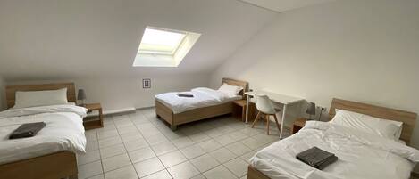 A dorm-style room with three beds, a desk, and a skylight.
