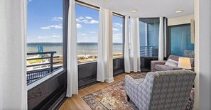 Una habitación con un ventanal grande con vistas a la playa, un sofá, un sillón estampado y una lámpara.