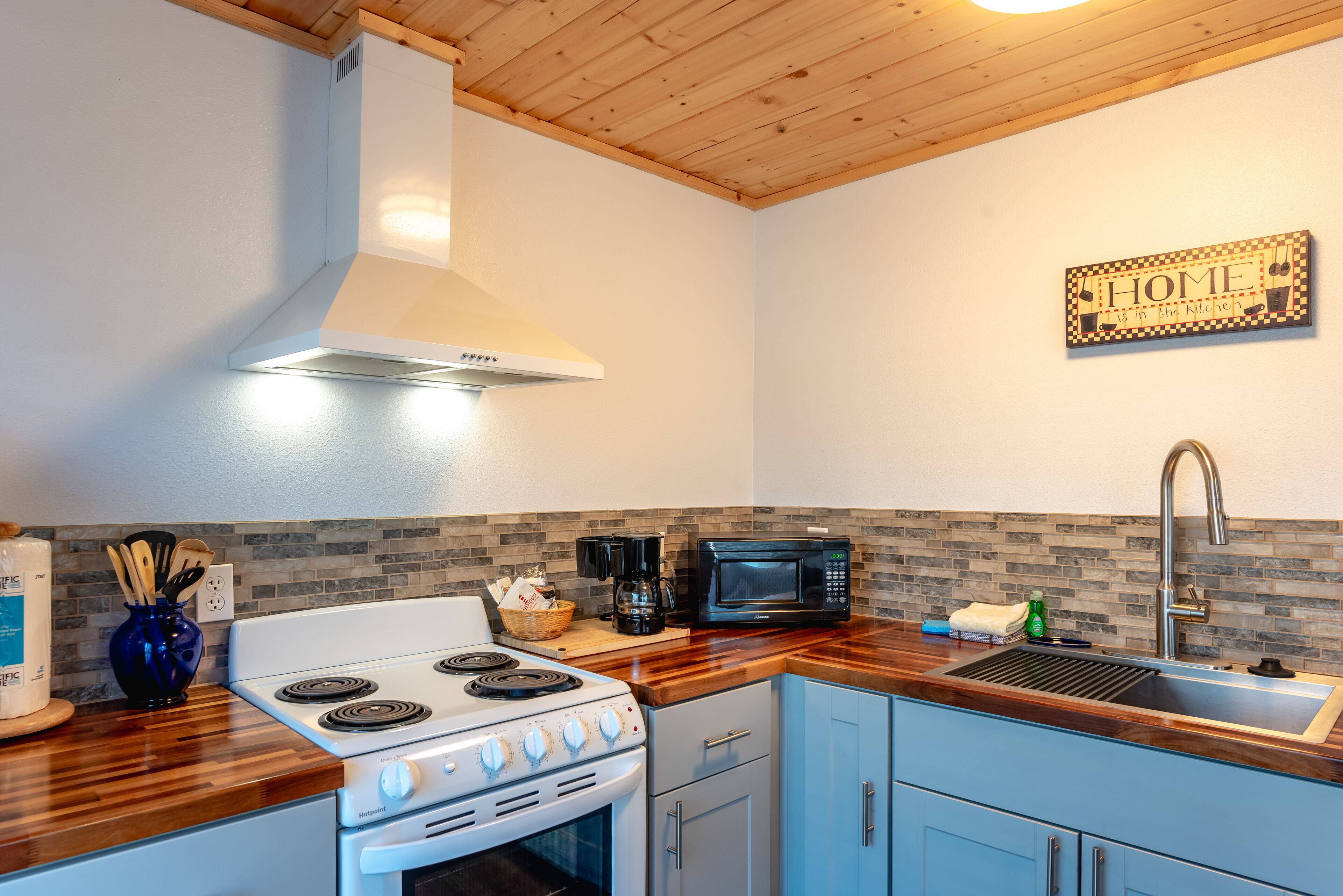 Una cocina con estufa blanca, microondas, lavabo y techo de madera.