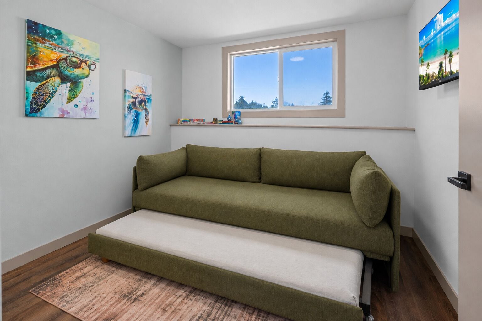 A room with a green sofa, a window with a view, and two artworks on the walls.
