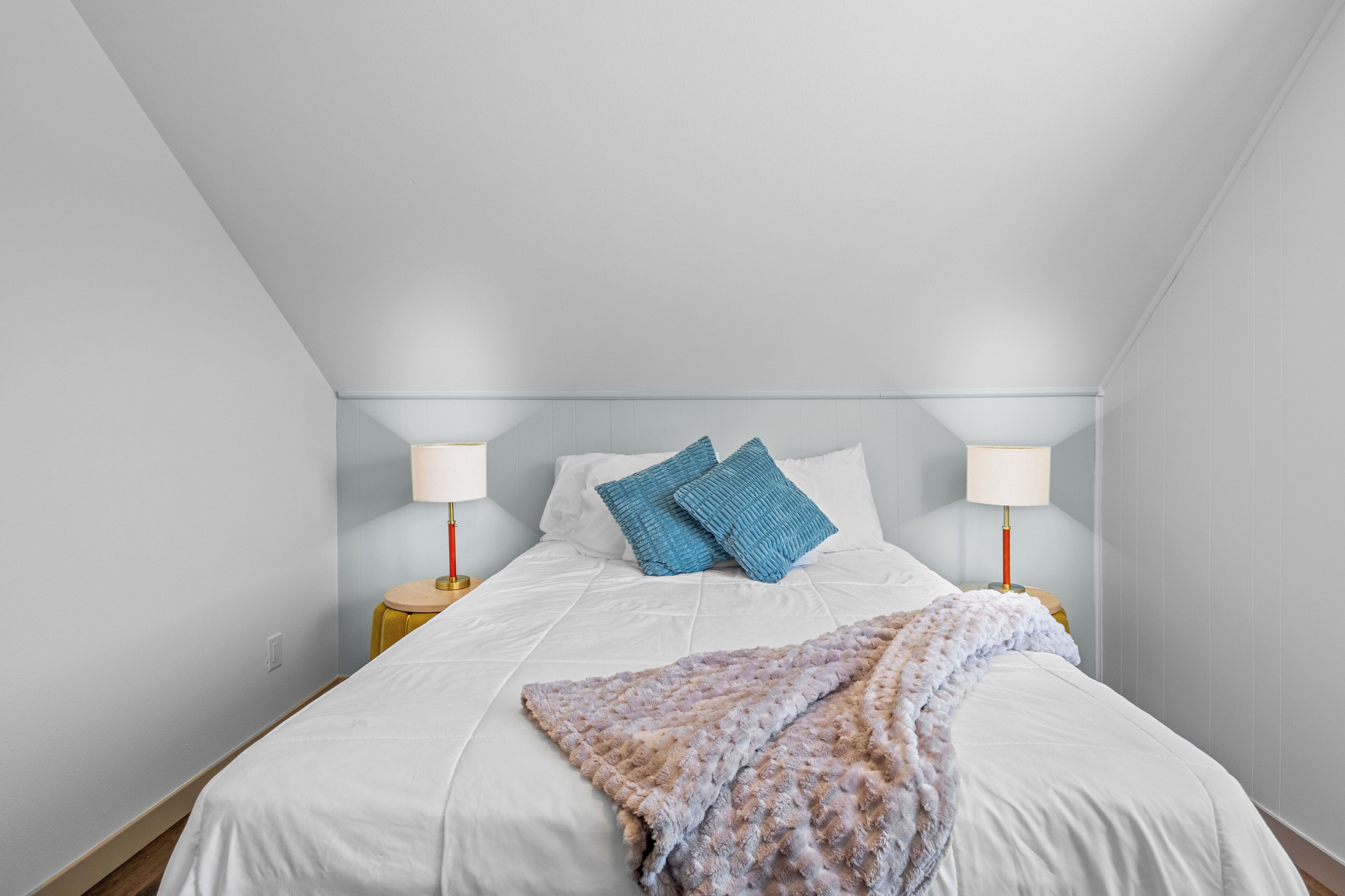 A bedroom with a single bed, two bedside lamps, and a blanket.