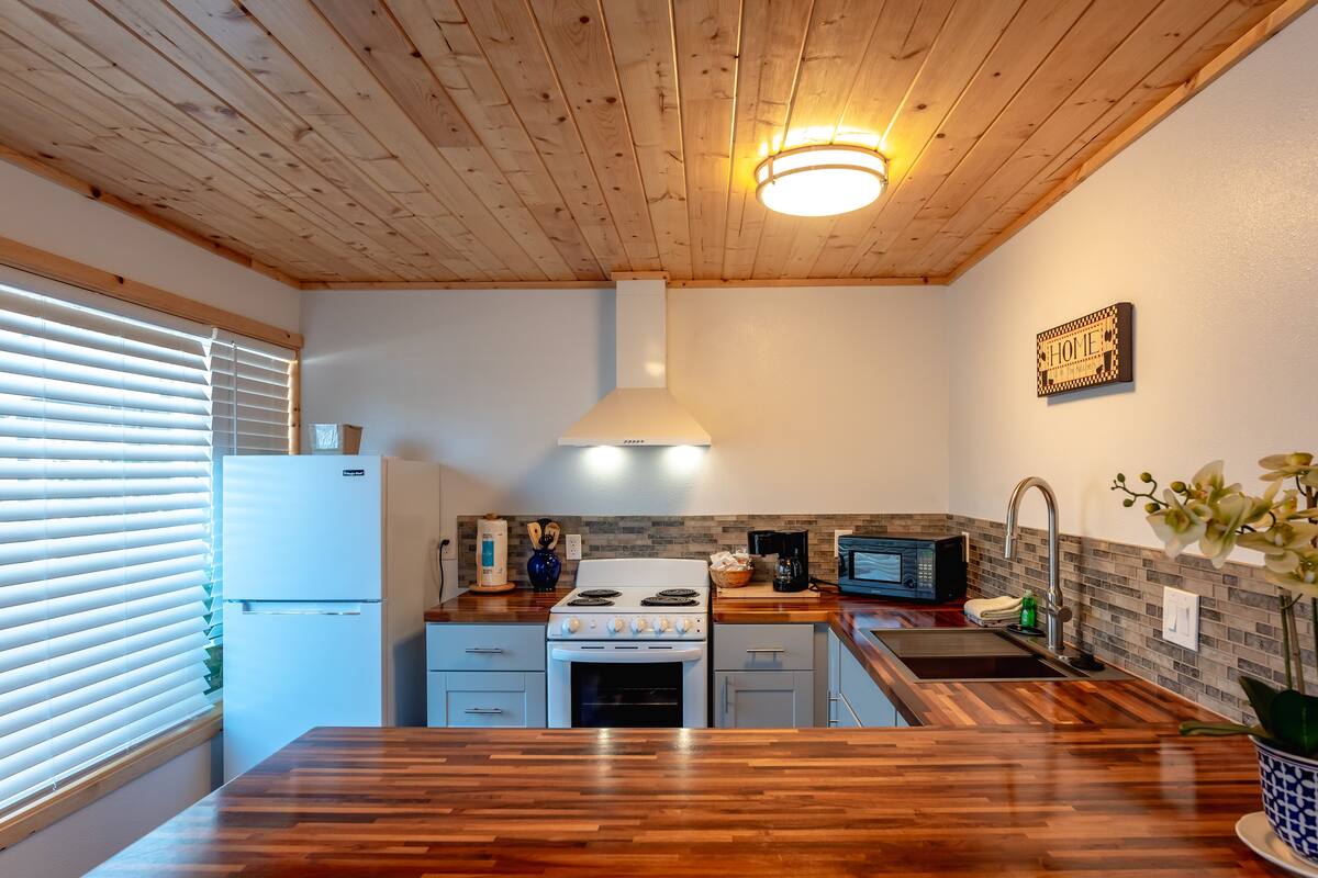 Eine Küche mit Holzboden, einem Herd, einem Kühlschrank, einer Mikrowelle und einem Spülbecken.