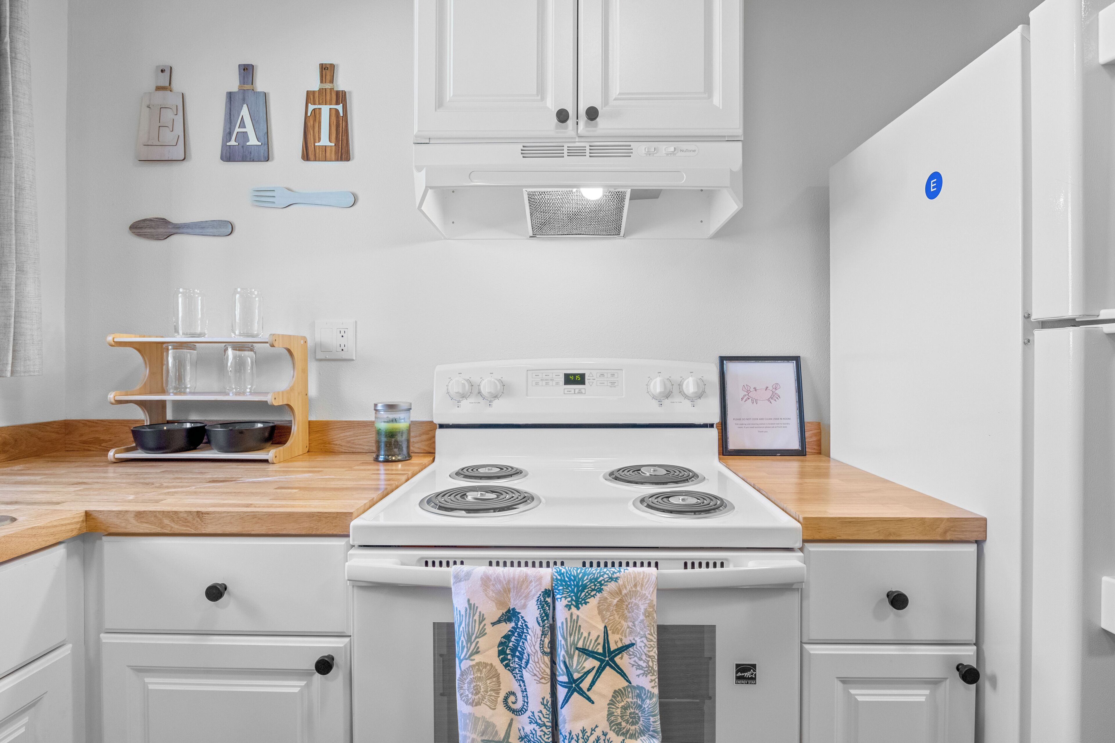 A kitchen with a white stove, wooden countertop, and cabinets. There are utensils hanging on the wall, a framed picture, and a small plant on the counter.