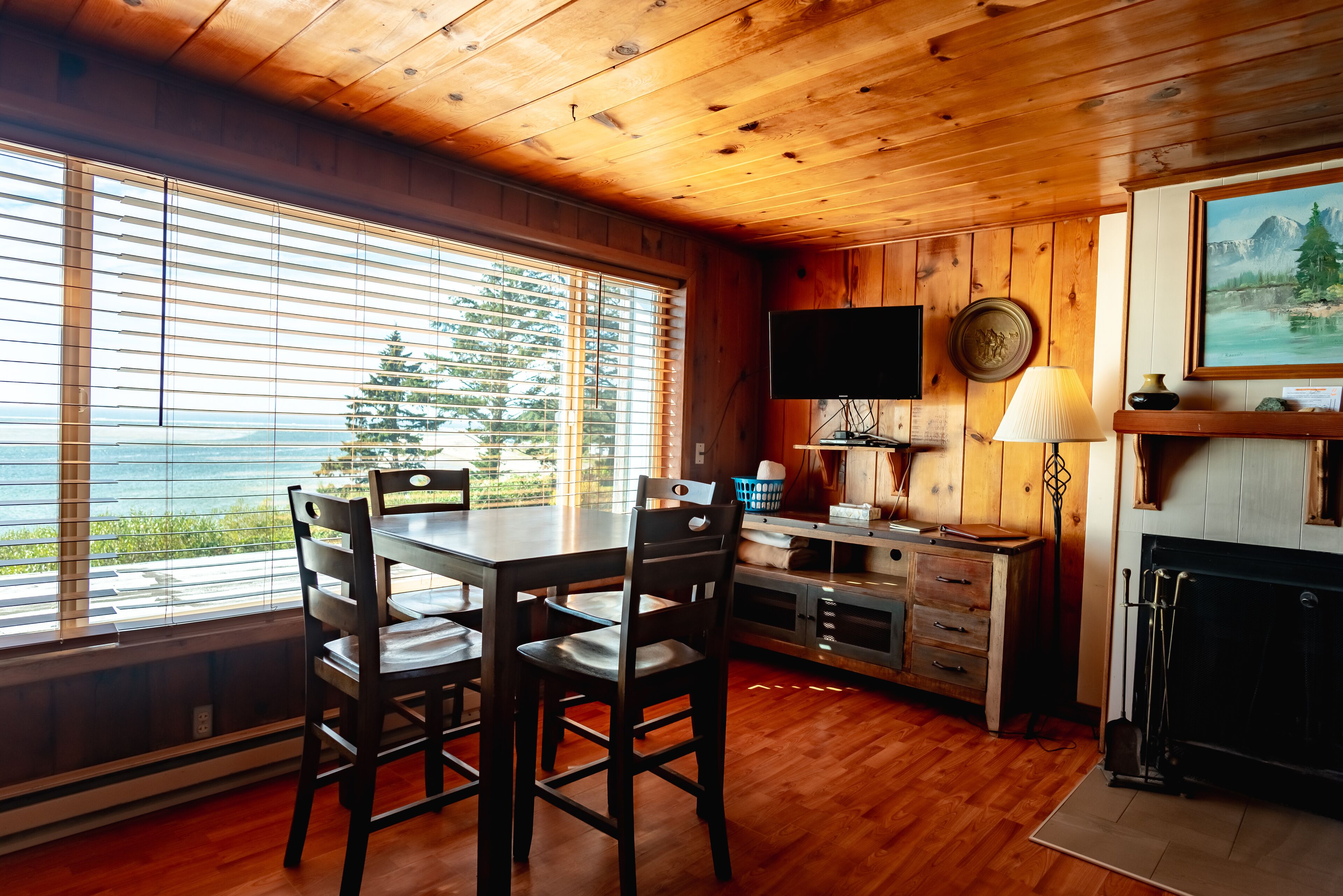 A wooden interior with a dining table and chairs, a TV mounted on the wall, and a fireplace.