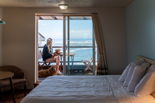 Une chambre d’hôtel avec un lit, une chaise, une table et une vue sur l’océan, accessible par une porte coulissante.