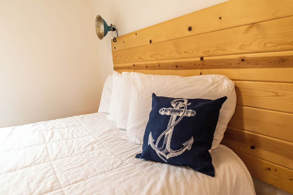 Ein Bett mit weißer Bettwäsche und einem dunkelblauen Kopfkissen mit Anker-Muster.