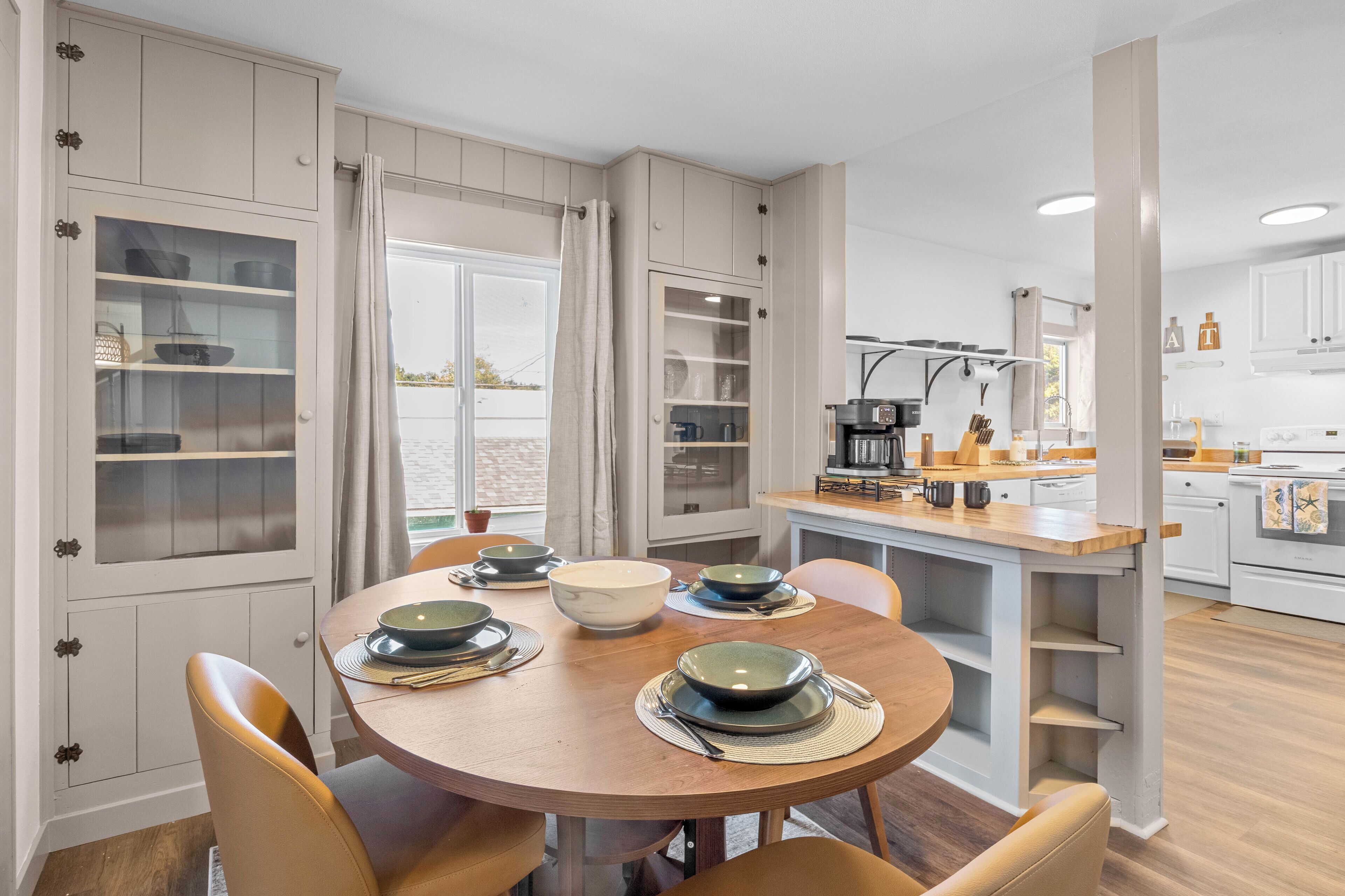 A dining area with a round table, chairs, and a kitchen in the background.
