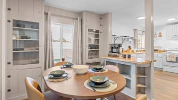 A dining area with a round table, chairs, and a kitchen in the background.