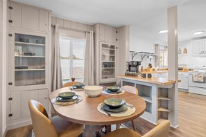 A dining area with a round table, chairs, and a kitchen in the background.
