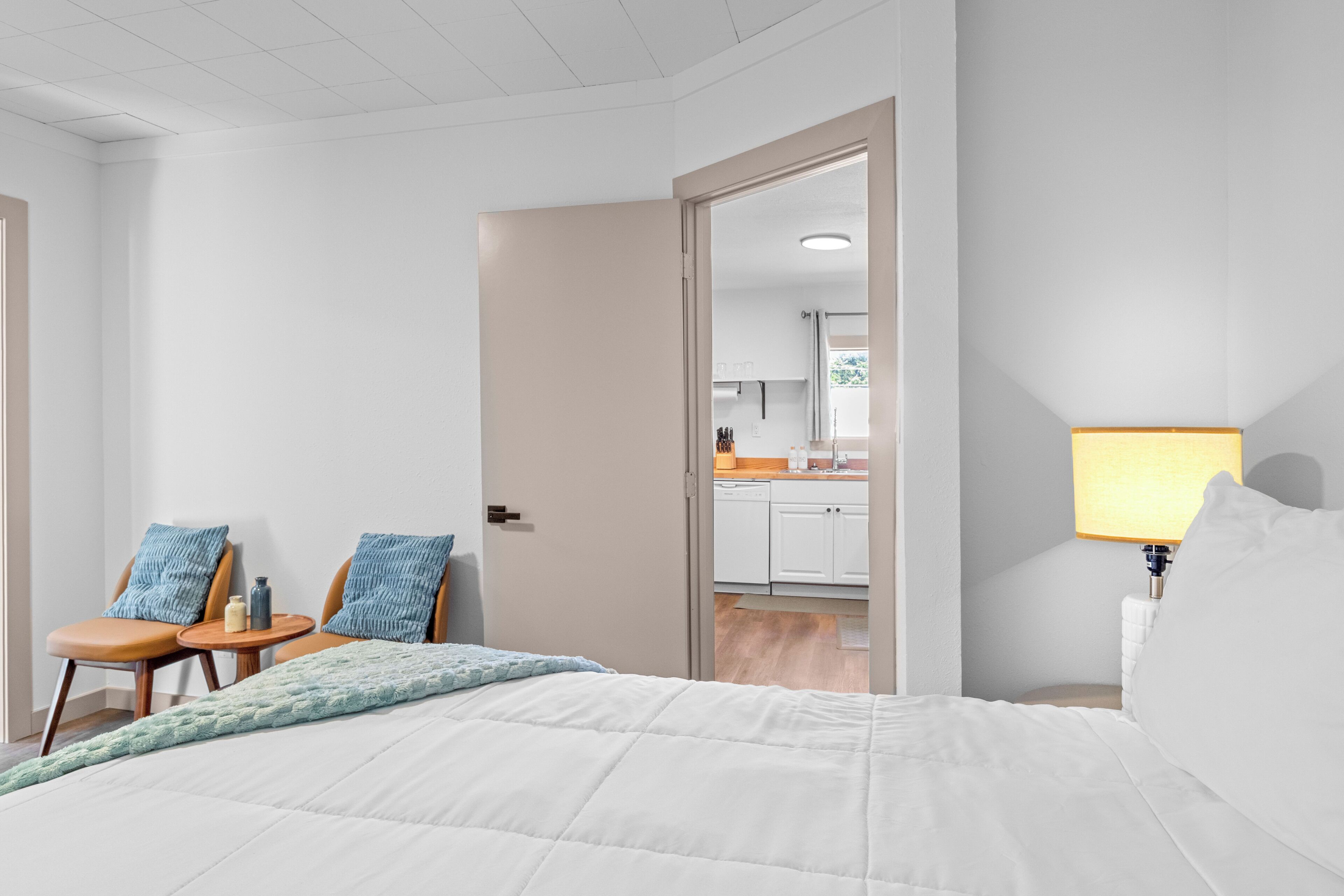 Habitación de hotel con cama, una silla, una mesita y vista a la cocina.