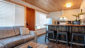 A cozy living room with a sofa, a coffee table, and a kitchen area with a bar stool and a refrigerator. - Terimore Bayfront Inn (Tillamook)