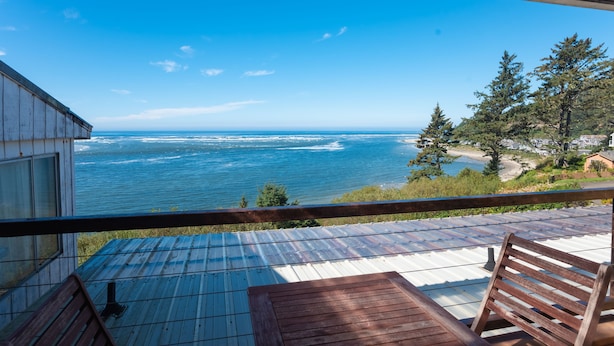 A wooden deck with a view of the ocean and a forested hillside. - Terimore Bayfront Inn (Tillamook)