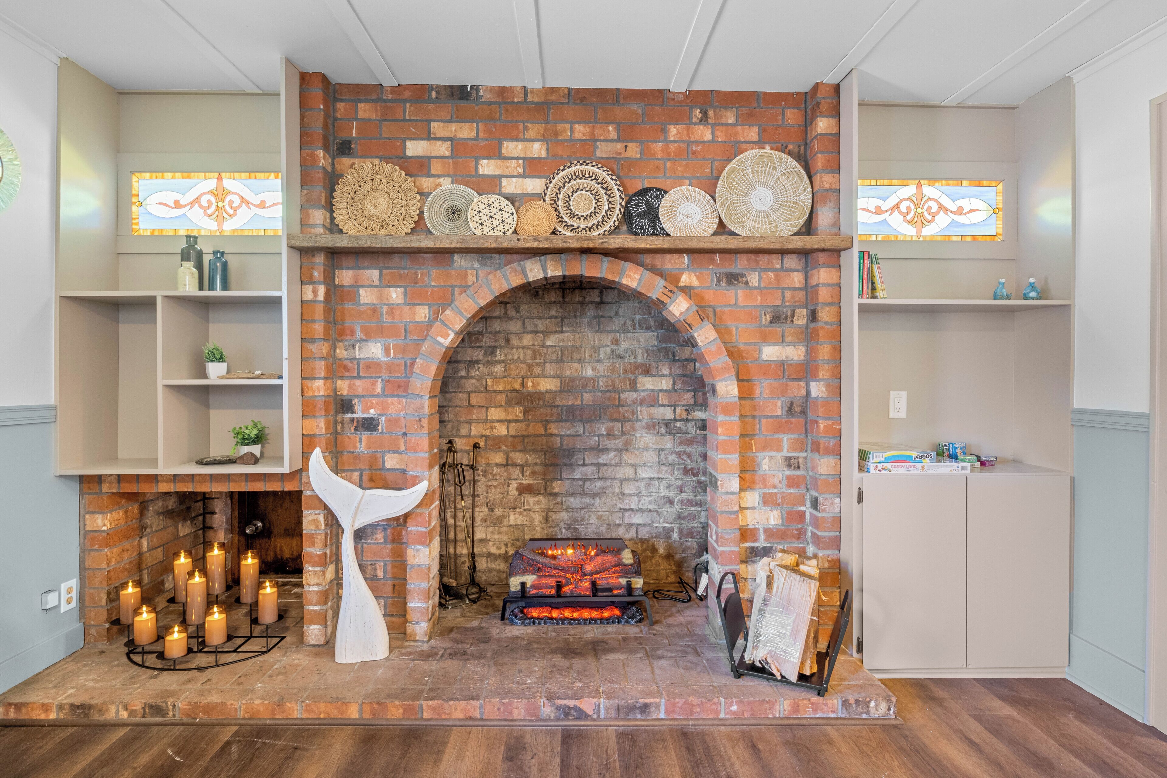 A brick fireplace with a mantel decorated with plates, surrounded by shelves with books and decorative items.