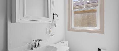 Un baño con lavamanos blanco, un espejo, un inodoro y una ventana con persianas.