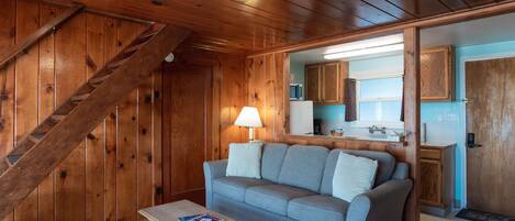 A wooden interior with a sofa, a table, and a staircase.