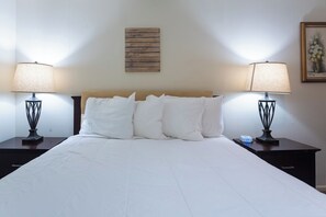 A neatly made bed with white linens, two bedside tables with lamps, and a wall-mounted sign.