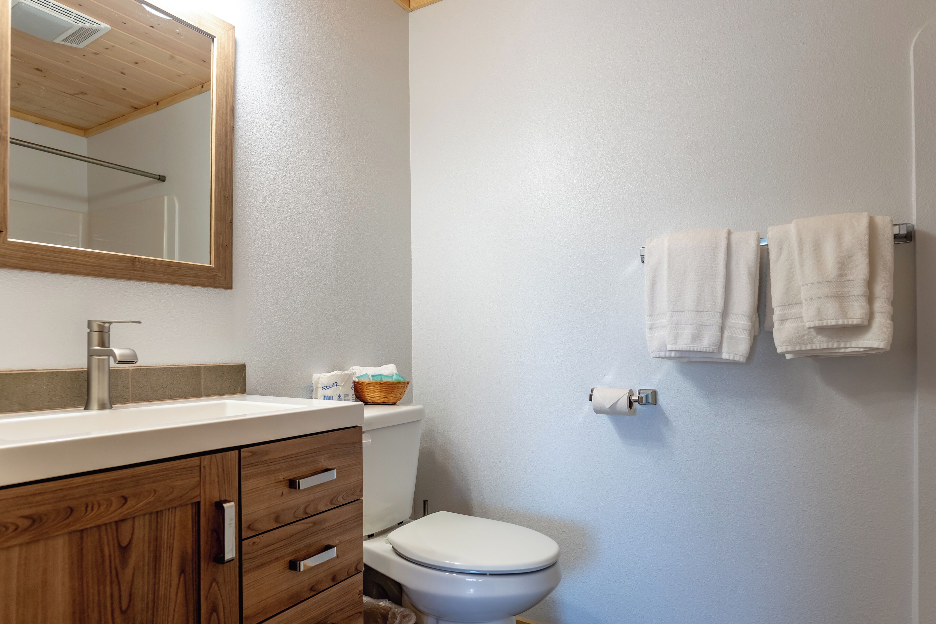 Un baño con tocador de madera, un lavabo blanco, un inodoro y un perchero para toallas.