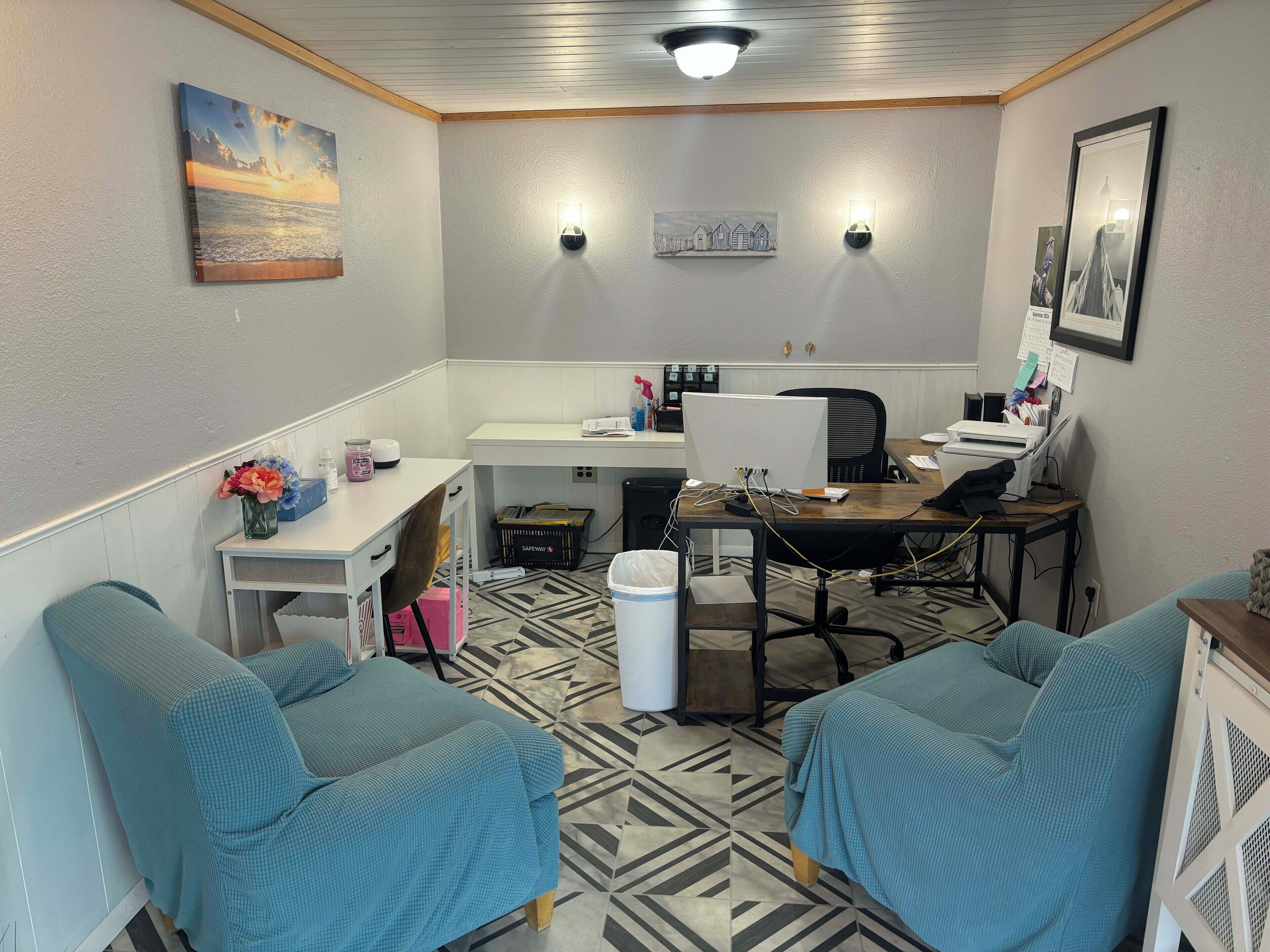 A small, well-lit room with a desk, computer, and two chairs.