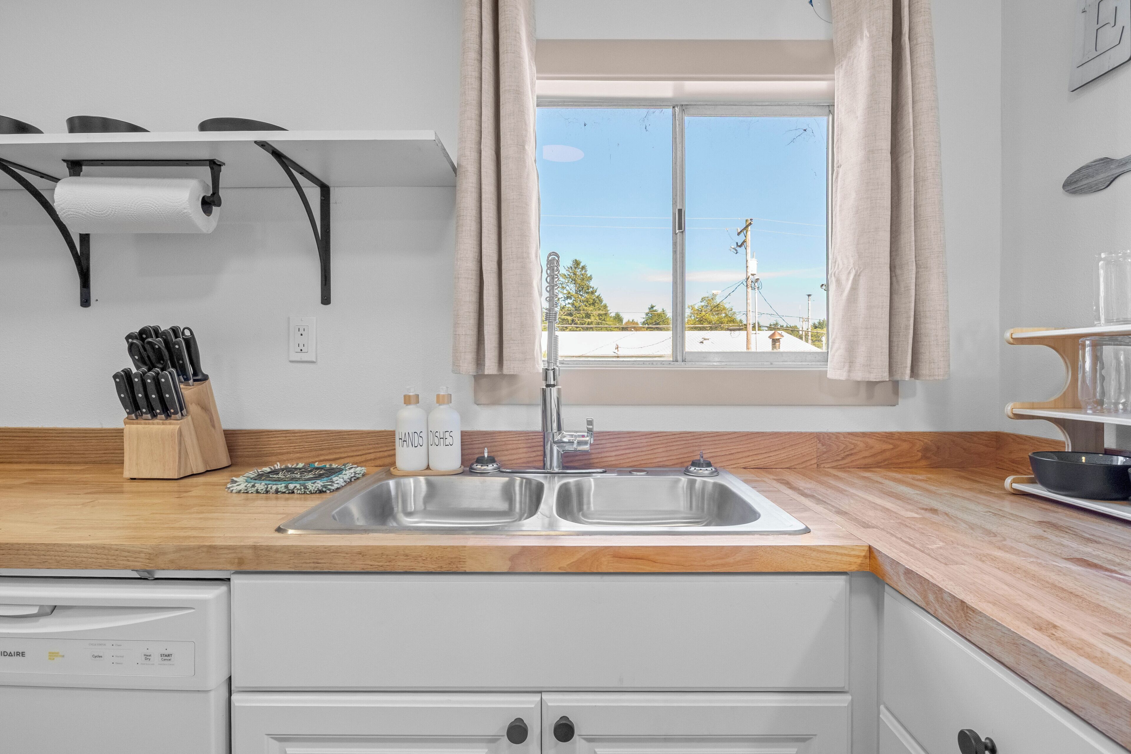 A kitchen with a double sink, a dish rack, and a window with curtains.