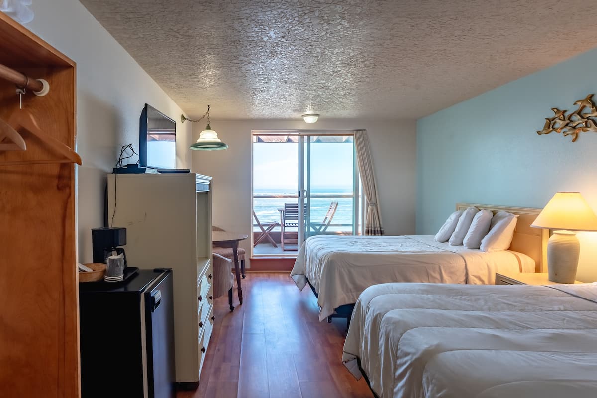 Ein Hotelzimmer mit zwei Betten, einem Schreibtisch mit Kaffeemaschine, einem Fernseher und Meerblick durch eine Schiebetür.