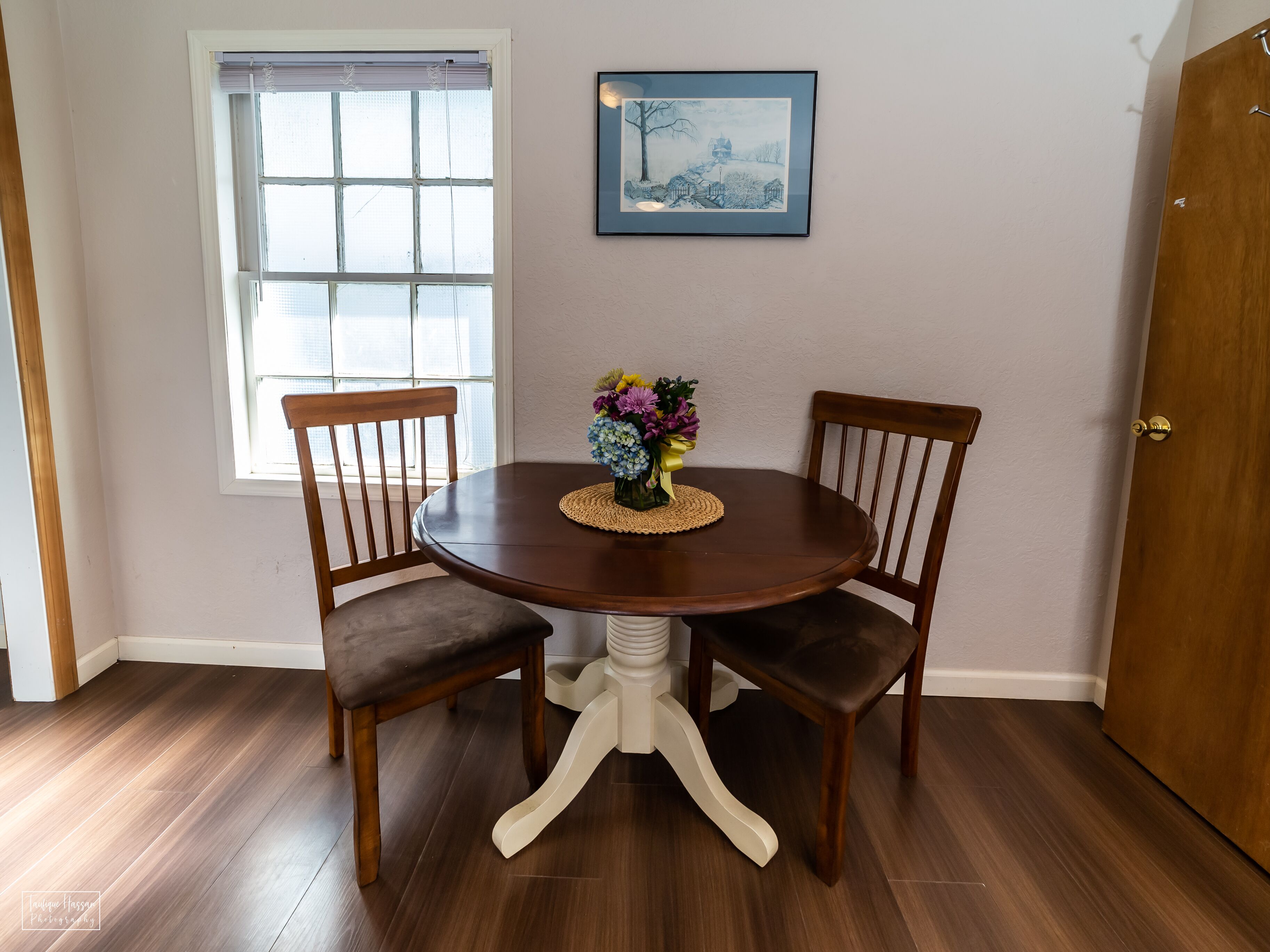 A dining area with a round table, two wooden chairs, and a vase of flowers.