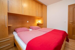 A single bed with a red and white checkered bedspread, wooden headboard, and a nightstand with drawers.