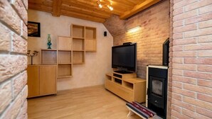 Un salon chaleureux avec un mur en briques, un plafond en bois, un téléviseur, une cheminée et des étagères intégrées.