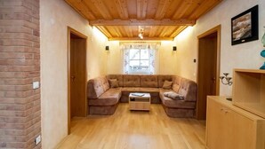 Une pièce chaleureuse avec un plafond en bois, un canapé d’angle marron, un meuble en bois et une fenêtre avec des rideaux.