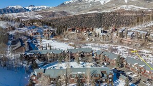 A ski resort with multiple buildings, including a lodge with a large roof and a parking area. - Mountain Vista: Beautiful Basecamp @ Meadows Lift (Mountain Village)