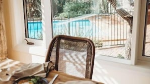 A dining table with plates of food, a chair, and a window with a view of a pool and trees. - Beautiful 5 Bedroom Home with Pool & Tennis Court (Orange)