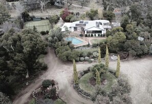 A residential property with a tennis court, swimming pool, and landscaped garden.
