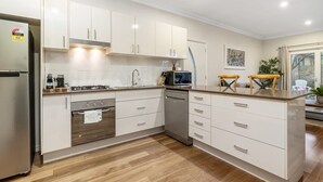 A modern kitchen with white cabinetry, a stainless steel refrigerator, a microwave, and a dishwasher. - Stylish Sale Street Studio - Walk to Town (Orange)