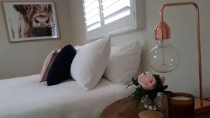 Une chambre à coucher avec un lit, une table de chevet avec une lampe, un vase de fleurs et un tableau encadré au mur.