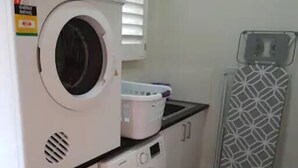 Un espace buanderie compact comprenant un lave-linge à chargement frontal, un sèche-linge et un étendoir.