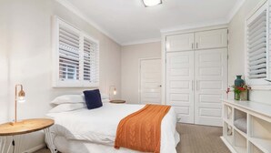 A bedroom with a bed, a bedside table, a lamp, a wardrobe, and a window with blinds. - Stylish Sale Street Studio - Walk to Town (Orange)