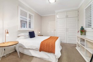 Ein Schlafzimmer mit Bett, Nachttisch, Lampe, Kleiderschrank und einem Fenster mit Jalousien.