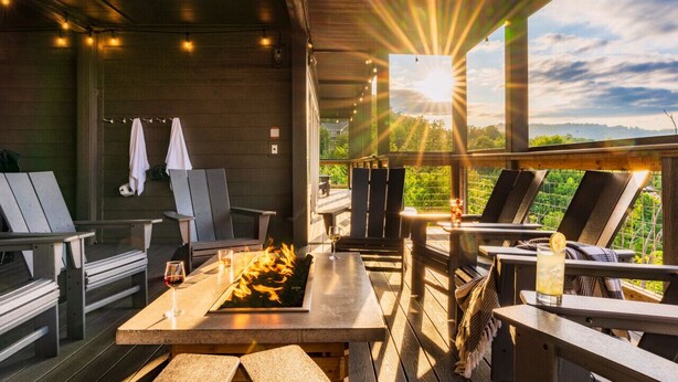 An outdoor seating area with wooden tables and chairs, a fire feature, and a view of the landscape. - Swim Spa/Luxe Design/Views/GameRoom/Theater - Bear Bottom (Gatlinburg)