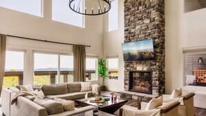 A spacious living room with a stone fireplace, large windows, and a cozy seating area. - Swim Spa/Luxe Design/Views/GameRoom/Theater - Bear Bottom (Gatlinburg)