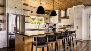 A modern kitchen with white cabinetry, a large island with bar stools, stainless steel appliances, and pendant lighting. - Swim Spa/Luxe Design/Views/GameRoom/Theater - Bear Bottom (Gatlinburg)