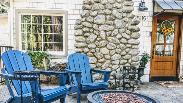 A stone wall, two blue Adirondack chairs, a fire pit, and a wooden door with a number plaque. - Charming Fox Cottage w/ Wood Burning Fireplace (Idyllwild-Pine Cove)