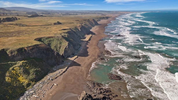 Un paysage côtier avec une plage de sable, des falaises rocheuses et des vagues de l’océan.