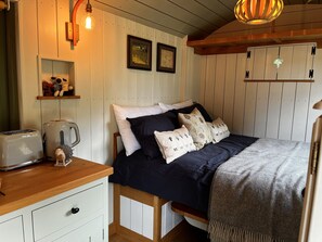 Un dormitorio acogedor con una cama de madera, una mesita de noche, un hervidor y un estante con adornos.