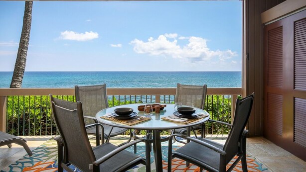 A round table with chairs on a balcony overlooking the ocean, with a view of the sea and sky. - Aloha Condos, Kanaloa at Kona, Condo 1901, Oceanfront, AC (Kailua Kona)