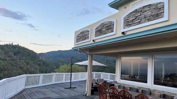 Una terraza de madera con muebles exteriores, una pared de acento de piedra y vistas a una ladera boscosa.