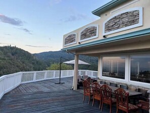 Une terrasse en bois avec des meubles d’extérieur, un mur décoratif en pierre et une vue sur une colline boisée.