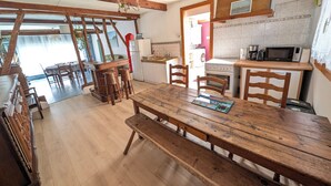 A rustic dining area with a wooden table and benches, a kitchen with basic appliances, and a view of the outdoors.
