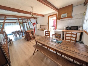 Un comedor rústico con una mesa y bancos de madera, una cocina con electrodomésticos básicos y vistas al exterior.