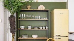 Un coin repas avec une table en bois, une chaise, un mur vert, un réfrigérateur de style vintage et une étagère contenant de la verrerie et de la vaisselle.