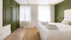 Une chambre avec un grand lit, des meubles verts, des rideaux blancs et un tapis tissé.