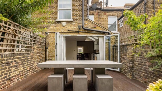 A concrete table with four legs on a wooden deck, surrounded by brick walls and a wooden fence.